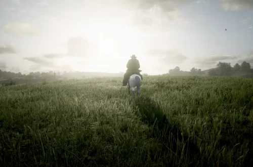 Arthur Morgan riding through a green field in the Heartlands towards the rising sun.