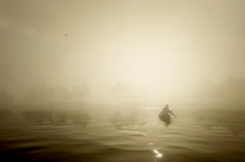 Arthur Morgan paddling a canoe on Flatiron Lake at sunset.